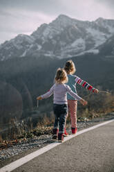 Playful girls with arms outstretched walking on road marking - OMIF00162