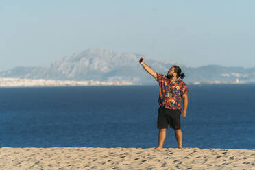 Junger Mann macht Selfie mit seinem Smartphone am Strand, Tarifa, Spanien - DAMF00898