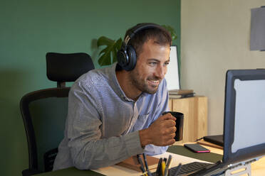 Smiling freelancer wearing headphones talking on video conference through laptop - VEGF05134