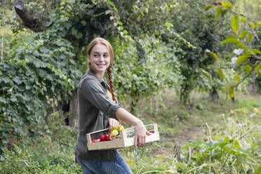 Smiling young female farmer with crate looking over shoulder - EIF02301