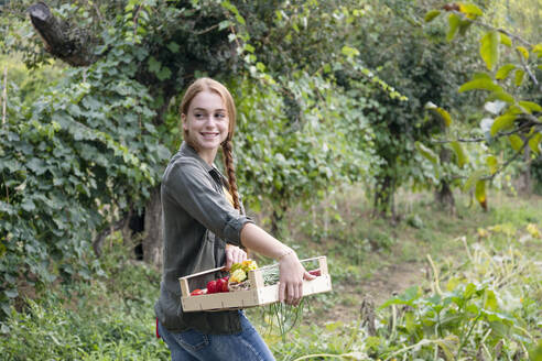 Lächelnde junge Bäuerin mit Kiste, die über die Schulter schaut - EIF02301