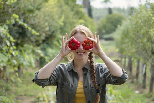 Playful female farmer holding tomatoes in front of eyes - EIF02304