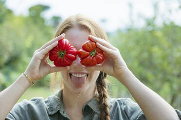 Playful female farmer holding tomatoes in front of eyes and sticking out tongue - EIF02305
