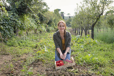 Smiling female farmer opening bean in community garden - EIF02312