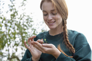 Lächelnde Bäuerin mit geflochtenem Haar, die eine Pflanze in der Hand berührt - EIF02318