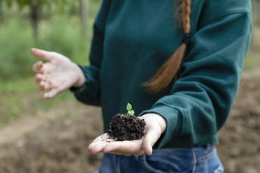 Female farmer holding new plant sprouting from soil - EIF02319