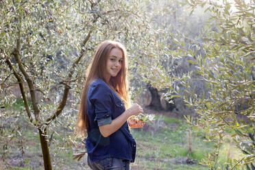 Lächelnde junge Frau mit langen Haaren inmitten von Olivenbäumen auf dem Lande - EIF02336