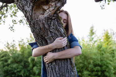 Young woman with eyes closed embracing tree - EIF02361