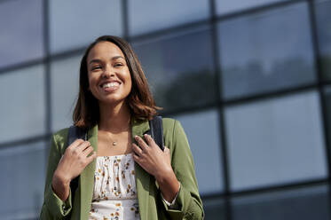 Smiling woman with backpack in front of glass - KIJF04274