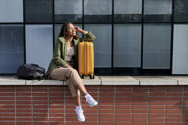 Woman with eyes closed leaning on wheeled luggage - KIJF04280