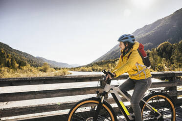 Woman with backpack riding mountain bike on bridge - UUF25024