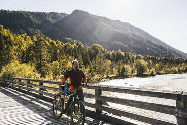 Smiling man wheeling mountain bike on bridge - UUF25025