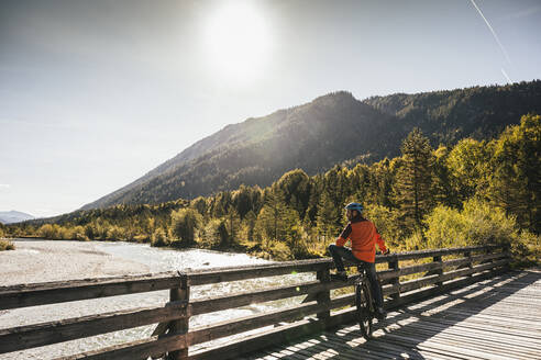 Mountainbiker mit Fahrrad mit Blick auf den Fluss an einem sonnigen Tag - UUF25032