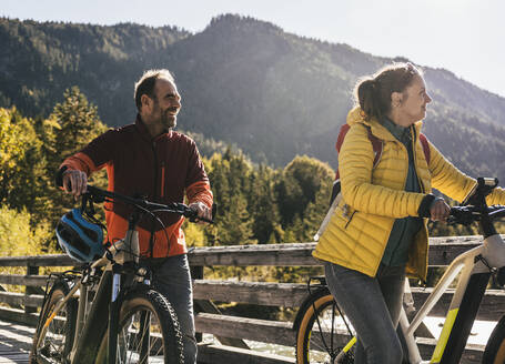 Smiling man wheeling bicycles with woman on bridge - UUF25038