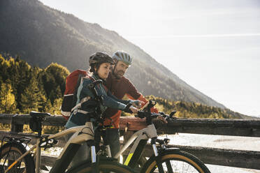 Couple pointing at mobile phone attached to bicycle on bridge - UUF25051