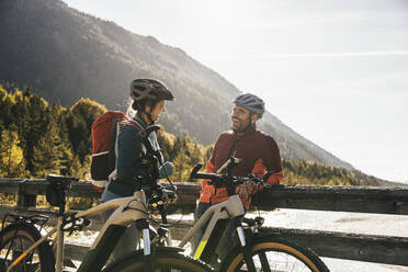 Smiling couple with bicycles talking on bridge - UUF25052