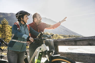 Smiling mature couple standing with bicycles on bridge - UUF25053