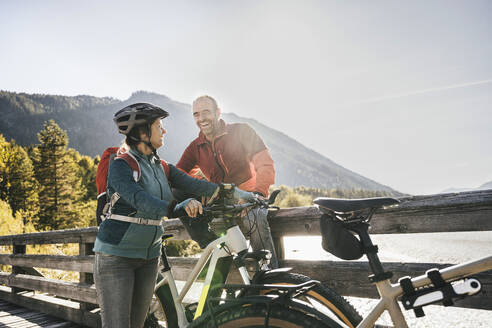 Smiling man looking at woman with cycling helmet on bridge - UUF25054
