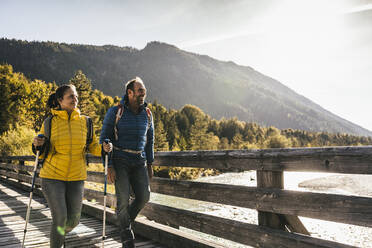 Lächelndes Paar mit Wanderstöcken auf einer Brücke - UUF25066