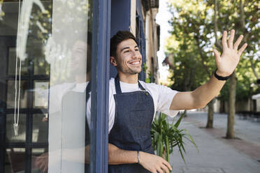 Smiling owner waving hand at cafe entrance - JCCMF04474