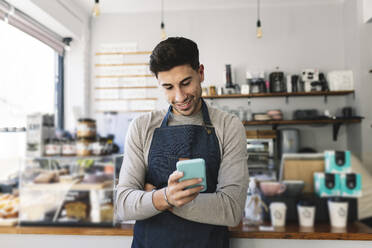 Waiter using smart phone in coffee shop - JCCMF04483