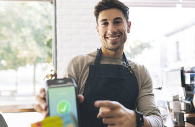 Waiter pointing at credit card reader screen in cafe - JCCMF04488