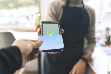 Cashier receiving payment through card reader in cafe - JCCMF04490