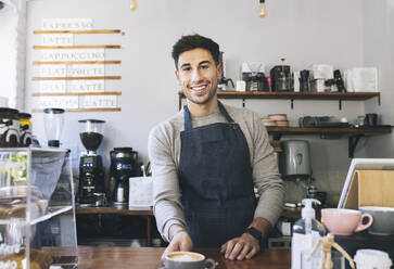 Lächelnder Kellner, der eine Kaffeetasse am Tresen eines Cafés reicht - JCCMF04491