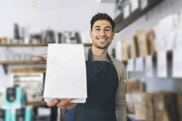 Smiling waiter holding credit card reader in cafe - JCCMF04494