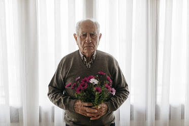 Senior man holding bouquet of daises at home - JRFF05194