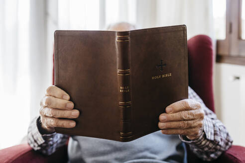 Senior man reading religious book at home - JRFF05198