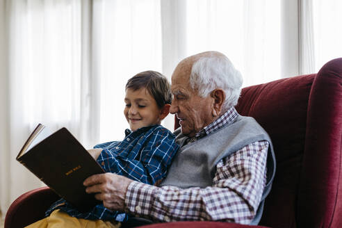 Grandfather reading bible with grandson at home - JRFF05199