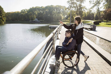 Girlfriend pointing while holding disabled boyfriend's hand at embankment - LLUF00292