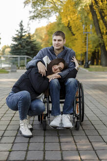 Young girlfriend leaning on disabled boyfriend's lap at park - LLUF00297