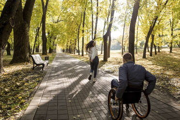 Freundin läuft mit behindertem Freund im Rollstuhl durch einen Park - LLUF00301