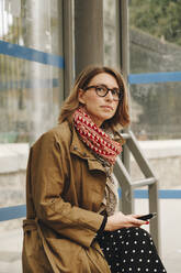 Woman with mobile phone waiting at bus stop - MRRF01649