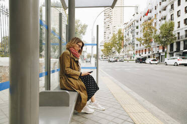 Woman using smart phone at bus stop - MRRF01650