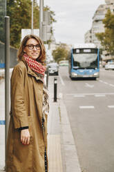 Lächelnde Frau an der Bushaltestelle an der Straße - MRRF01651