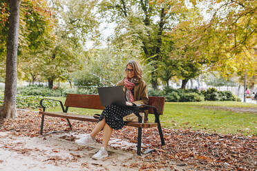 Smiling businesswoman using laptop on bench - MRRF01657