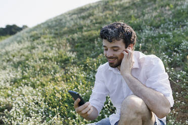 Smiling man using smart phone on meadow - TYF00001