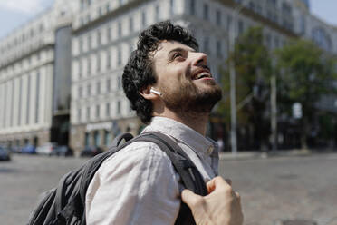 Happy man with backpack looking up in city - TYF00014
