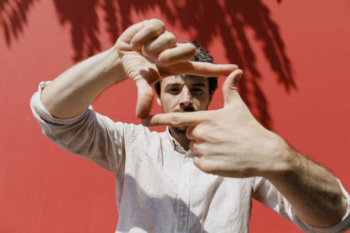 Man looking through finger frame in front of red wall - TYF00015