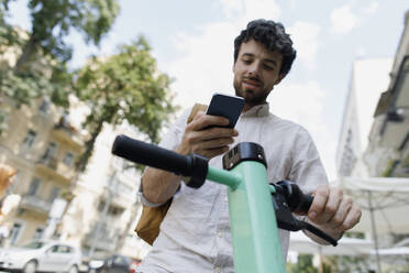 Man unlocking scooter with mobile phone in city - TYF00017