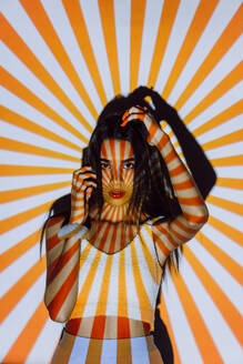 Coole junge ethnische Frau in Crop Top mit Streifen auf dem Körper von Projektor Licht Blick auf die Kamera - ADSF31399