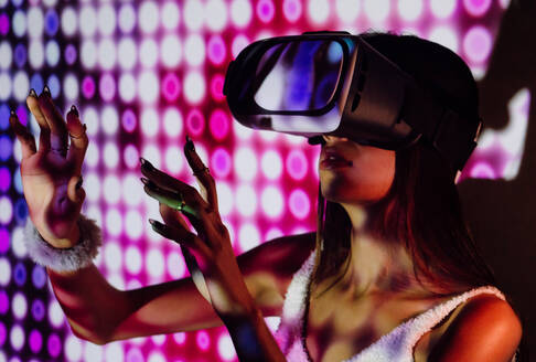 Fokussierte Frau mit Schatten auf dem Körper, die virtuelle Realität in einem modernen Headset bei Projektorlicht erlebt - ADSF31401