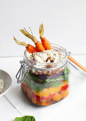 Salat mit bunten reifen gehackten Paprika und Bulgur mit rohen Karotten in einem Glas auf dem Tisch vor weißem Hintergrund serviert - ADSF31424