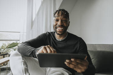 Lächelnder junger Mann mit Tablet-PC auf dem Sofa - MFF08283