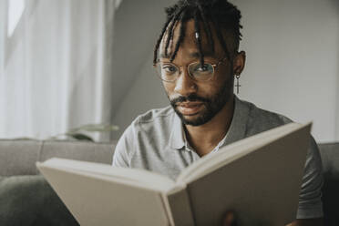 Young man wearing eyeglasses holding book at home - MFF08302