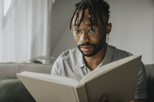 Junger Mann mit Brille hält Buch zu Hause - MFF08302