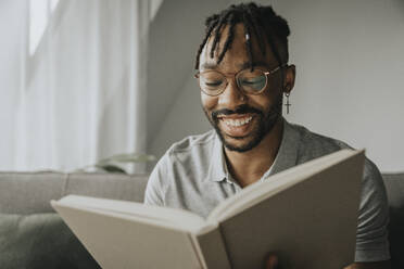 Glücklicher Mann mit Brille liest zu Hause ein Buch - MFF08303